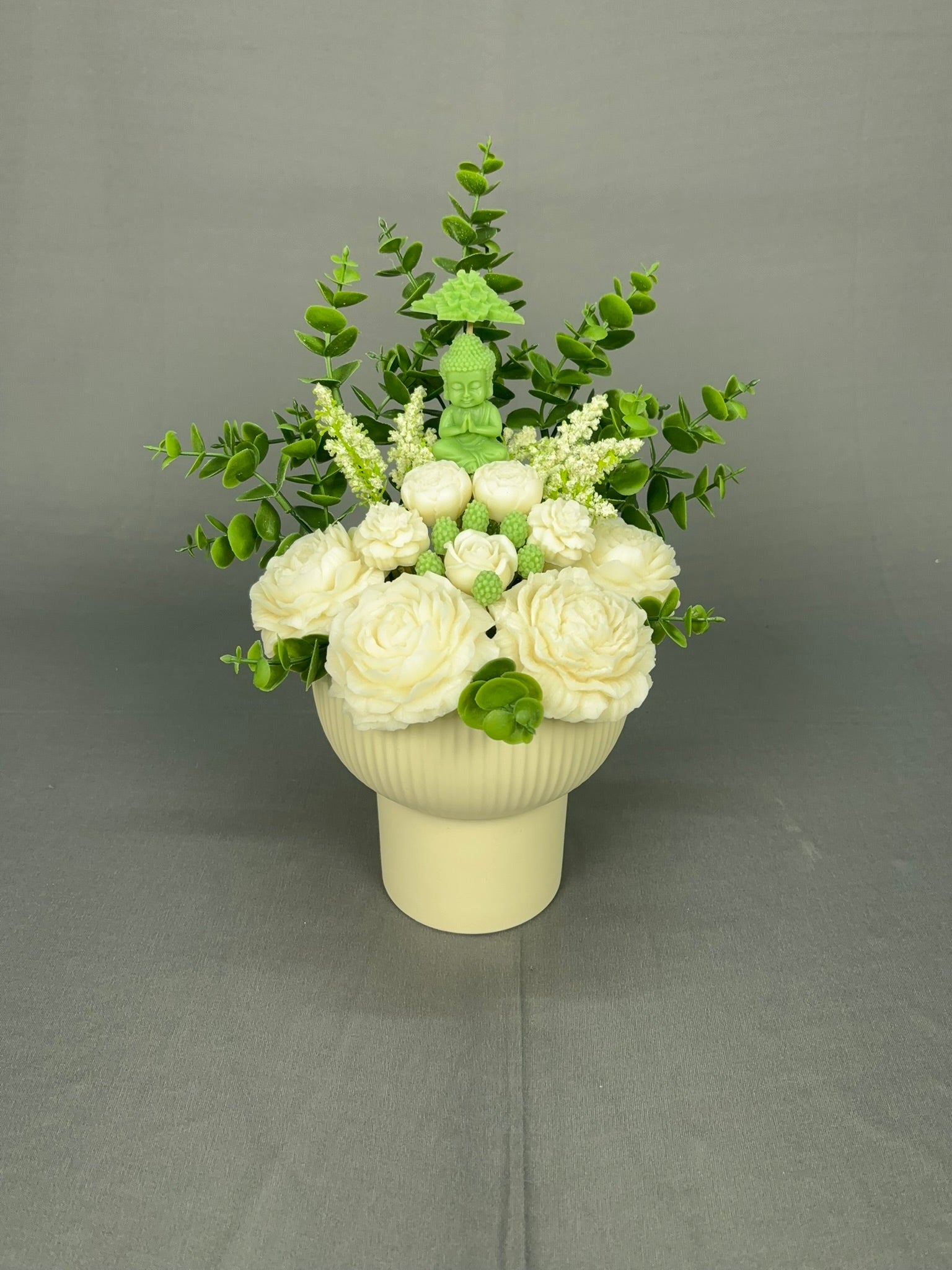 Buddha Peace candle bouquet with green Buddha centerpiece, white flowers, lush green foliage in a white ribbed ceramic pot