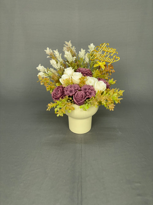 Mauve Magic candle bouquet with mauve and ivory flowers, happy birthday topper, white fillers and greenery in a cream ribbed ceramic pot
